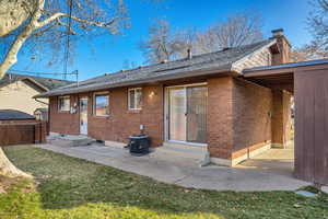 Rear view of house featuring entry steps, brick siding, roof with shingles, and a chimney