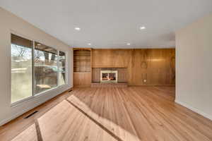 Unfurnished living room with light wood-style floors, a brick fireplace, built in features, recessed lighting, and wood walls