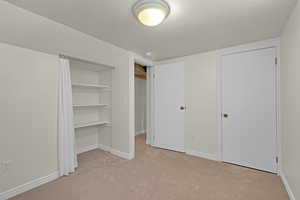 Unfurnished bedroom featuring a textured ceiling, light colored carpet, and a closet