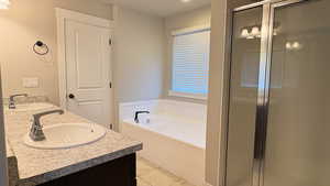 Full bathroom featuring double vanity, a stall shower, a garden tub, and light tile patterned floors
