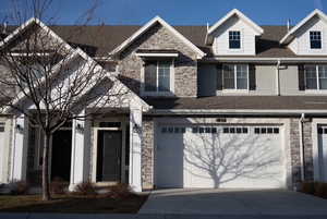 View of front facade with stone siding, an attached garage, driveway, and roof with shingles