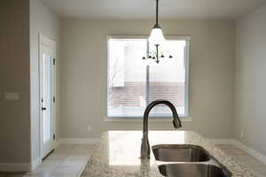 Kitchen featuring pendant lighting, light tile patterned floors, light stone countertops, and a chandelier