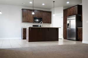 Kitchen featuring a kitchen bar, light tile patterned floors, hanging light fixtures, stainless steel fridge, and a center island with sink