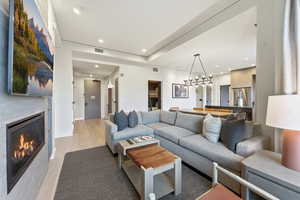 Living area featuring light wood-type flooring, recessed lighting, a glass covered fireplace, and a chandelier