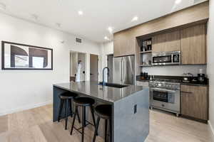 Kitchen featuring open shelves, dark stone counters, a kitchen breakfast bar, high end appliances, and modern cabinets