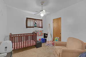 Carpeted bedroom featuring a crib and ceiling fan
