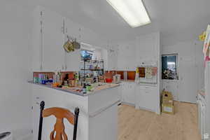 Kitchen with white cabinetry, white oven, light wood finished floors, light countertops, and a peninsula