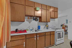 Kitchen featuring white range with gas cooktop, tile counters, brown cabinetry, and backsplash