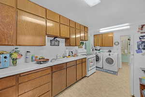 Kitchen with white appliances, brown cabinets, decorative backsplash, tile counters, and washing machine and clothes dryer