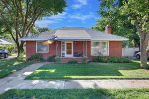 Bungalow-style home with a porch, a chimney, brick siding, and a shingled roof