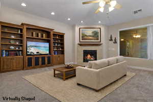 Living room featuring light colored carpet, ceiling fan, a high end fireplace, and recessed lighting. Virtually Staged.