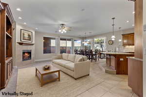 Living room featuring a tiled fireplace, recessed lighting, light tile patterned floors, a chandelier, and ceiling fan. Virtually Staged.