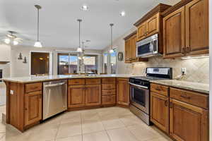 Kitchen featuring brown cabinetry, stainless steel appliances, light stone countertops, a peninsula, and recessed lighting