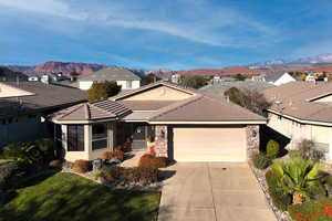 Single story home with stone siding, a garage, driveway, a front lawn, and a mountain view