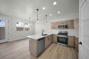 Kitchen featuring appliances with stainless steel finishes, light stone counters, a peninsula, hanging light fixtures, and light wood finished floors