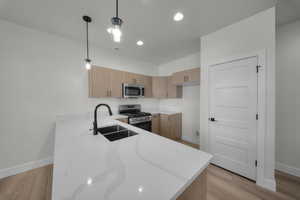 Kitchen featuring pendant lighting, light stone countertops, appliances with stainless steel finishes, modern cabinets, and light wood finished floors