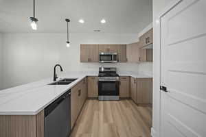 Kitchen featuring appliances with stainless steel finishes, a peninsula, brown cabinetry, light wood finished floors, and hanging light fixtures
