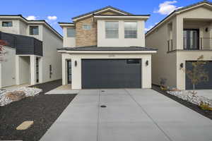 View of front facade with stucco siding, stone siding, driveway, and an attached garage