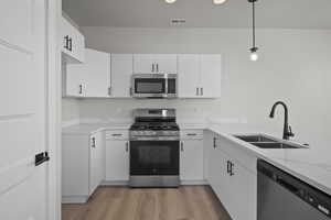Kitchen with appliances with stainless steel finishes, white cabinetry, pendant lighting, and light stone countertops