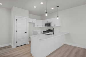 Kitchen featuring pendant lighting, white cabinets, appliances with stainless steel finishes, a peninsula, and light wood-style floors
