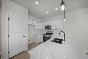 Kitchen with appliances with stainless steel finishes, pendant lighting, white cabinetry, light stone countertops, and light wood-style flooring