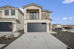 Modern home with stone siding, stucco siding, a garage, a balcony, and concrete driveway