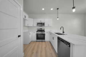 Kitchen featuring appliances with stainless steel finishes, white cabinetry, a peninsula, light wood-style floors, and pendant lighting