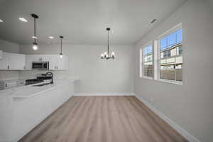 Kitchen featuring white cabinets, decorative light fixtures, appliances with stainless steel finishes, a peninsula, and a chandelier