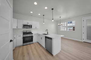 Kitchen with appliances with stainless steel finishes, a peninsula, white cabinetry, light wood-style floors, and decorative light fixtures