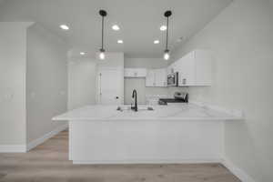 Kitchen featuring light wood-type flooring, white cabinets, hanging light fixtures, a peninsula, and appliances with stainless steel finishes