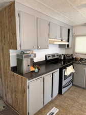 Kitchen with stainless steel range with electric cooktop, dark countertops, under cabinet range hood, gray cabinetry, and a textured ceiling