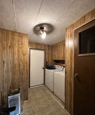 Laundry area with a textured ceiling, wooden walls, and separate washer and dryer