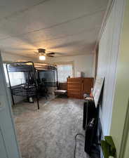 Carpeted bedroom with a ceiling fan and wood walls