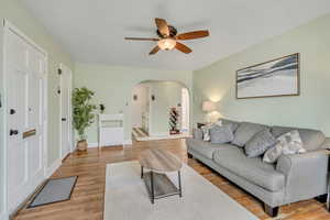 Living room featuring arched walkways, light wood-style flooring, and a ceiling fan