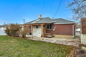 Back of property with brick siding, roof with shingles, a gate, and a chimney