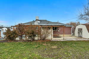 Back of house with a storage shed, a patio, brick siding, and roof with shingles