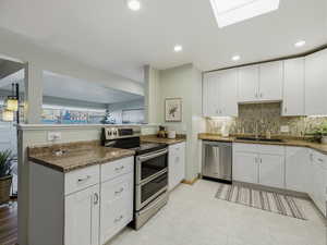 Kitchen featuring appliances with stainless steel finishes, white cabinetry, a peninsula, a skylight, and recessed lighting