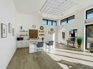 Kitchen with white cabinets, open shelves, light wood-type flooring, a high ceiling, and a breakfast bar area