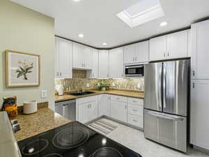 Kitchen featuring stainless steel appliances, dark stone countertops, white cabinetry, decorative backsplash, and recessed lighting