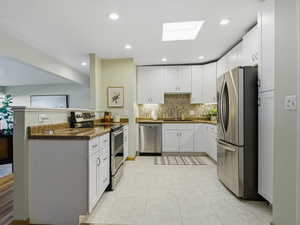 Kitchen featuring a skylight, appliances with stainless steel finishes, white cabinets, and recessed lighting