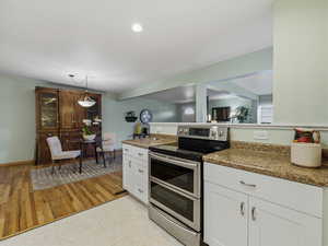 Kitchen featuring range with two ovens, white cabinets, light wood-style floors, hanging light fixtures, and light stone counters