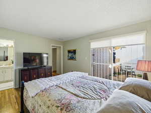 Bedroom with a textured ceiling, hardwood / wood-style flooring, access to exterior, and ensuite bath