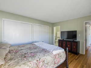 Bedroom featuring multiple closets, hardwood / wood-style floors, a textured ceiling, and ensuite bathroom