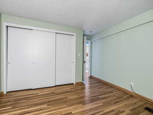 Unfurnished bedroom with a textured ceiling, wood finished floors, and a closet