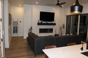 Living area with a large fireplace, a ceiling fan, wood finished floors, and recessed lighting
