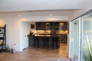 Indoor wet bar featuring dark countertops, light wood-style floors, open shelves, dark brown cabinetry, and recessed lighting