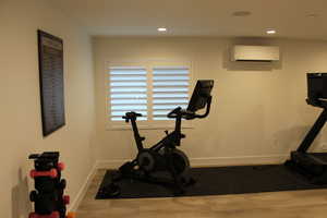 Workout area featuring wood finished floors, a wall unit AC, and recessed lighting
