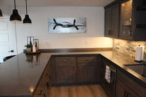 Kitchen featuring glass insert cabinets, dark brown cabinets, a peninsula, decorative light fixtures, and light wood finished floors