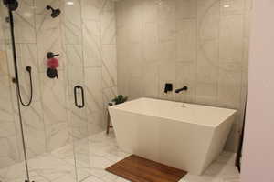 Bathroom with a marble finish shower, a soaking tub, tile walls, and light marble finish flooring