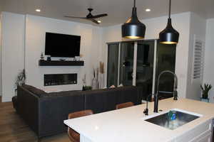 Kitchen featuring a ceiling fan, white cabinetry, a large fireplace, a kitchen island with sink, and hanging light fixtures